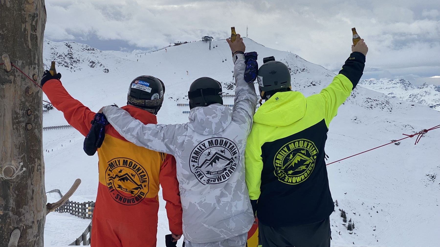 Tre amici con le tute Family Mountain brindano davanti alle cime innevate